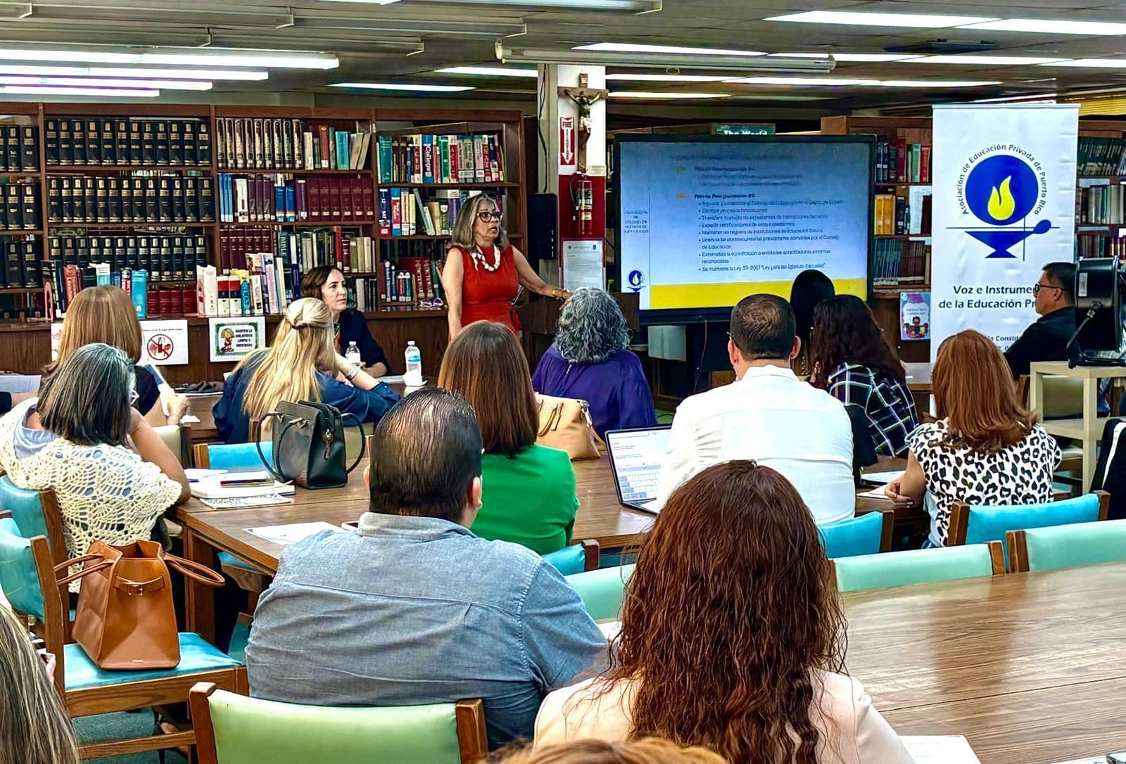 Directores de escuelas en un taller de la AEP en una biblioteca, junto al estandarte de la Asociación